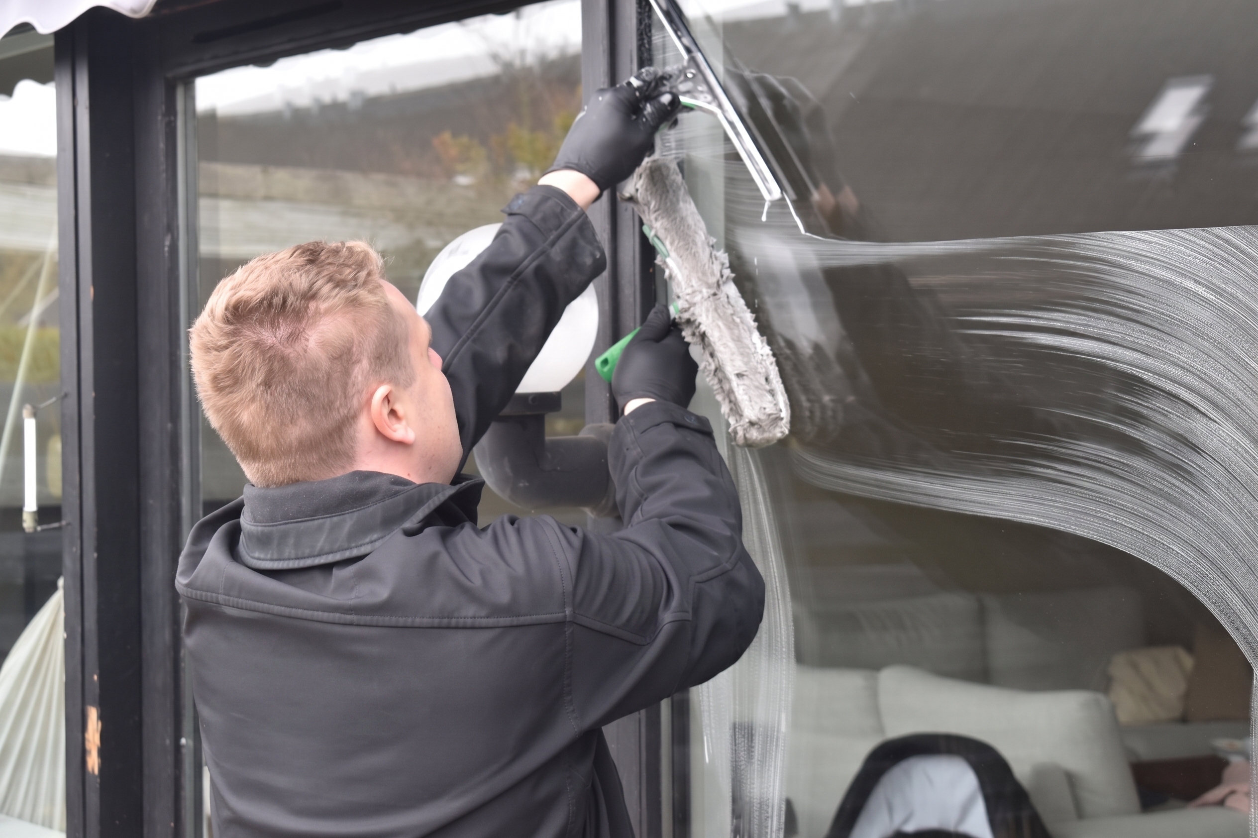 Professional exterior cleaner washing a large residential window
